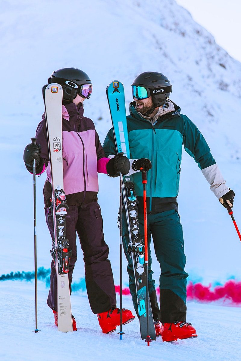 Twee skiërs met helm en skibril staan aan de pisterand in Obertauern en houden hun ski's rechtop naast zich