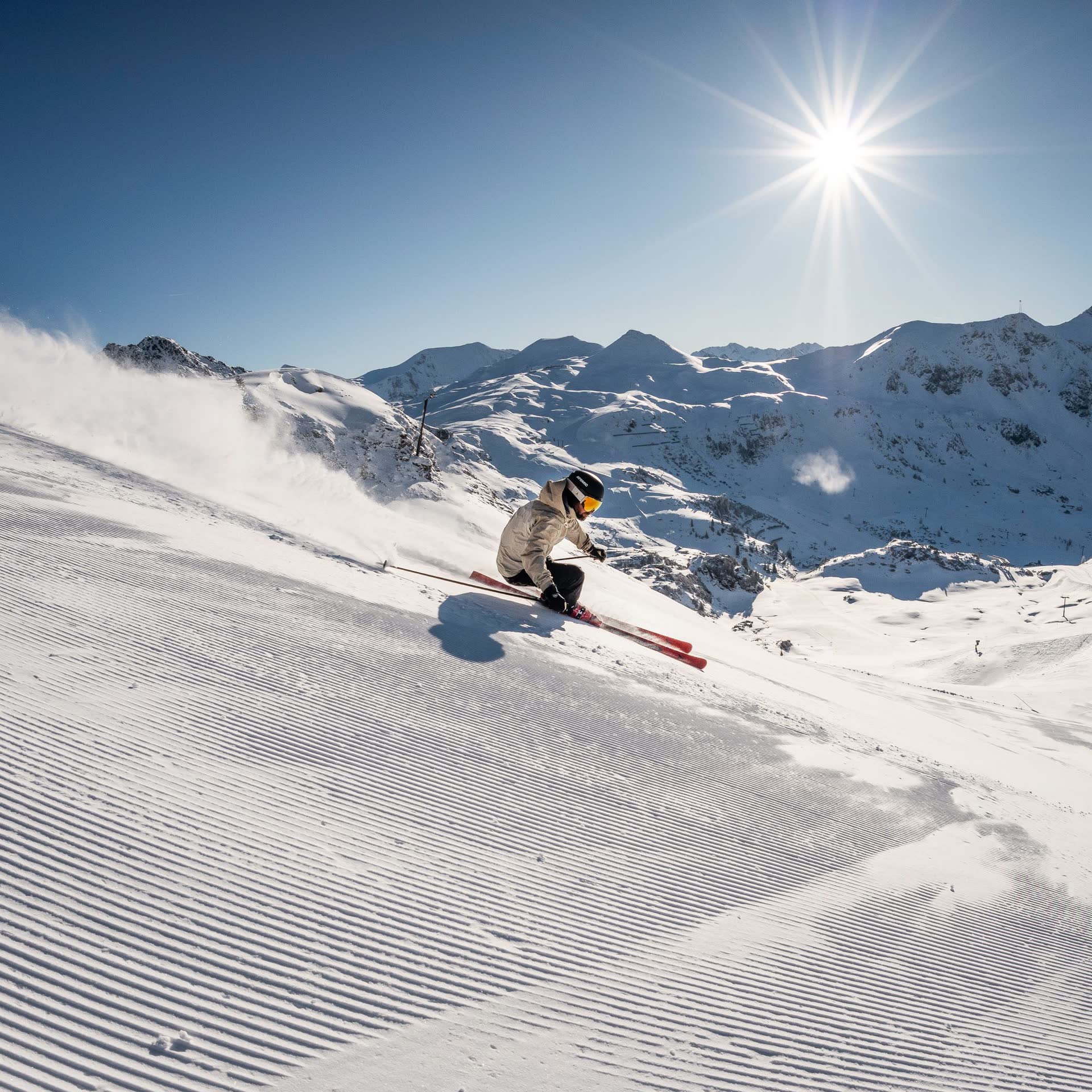 Skiër in een beige jas aan het carven op een geprepareerde piste in Obertauern